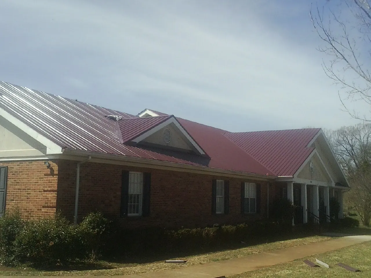 Red metal roof with gabled entries on a long brick building, from a Hail Damage Roof Repair job in Woods Cross