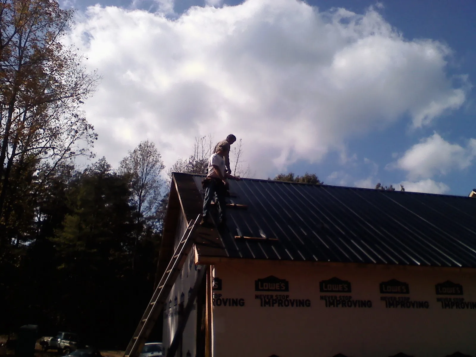 Roofer fastening dark metal panels high against a cloudy sky, from a Roof Inspection job in Woods Cross