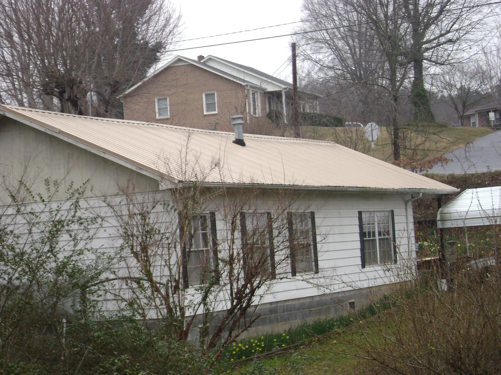 Tan metal roof on a white sided house set into a hillside — Commercial Roofing by Roofing Brothers in Woods Cross