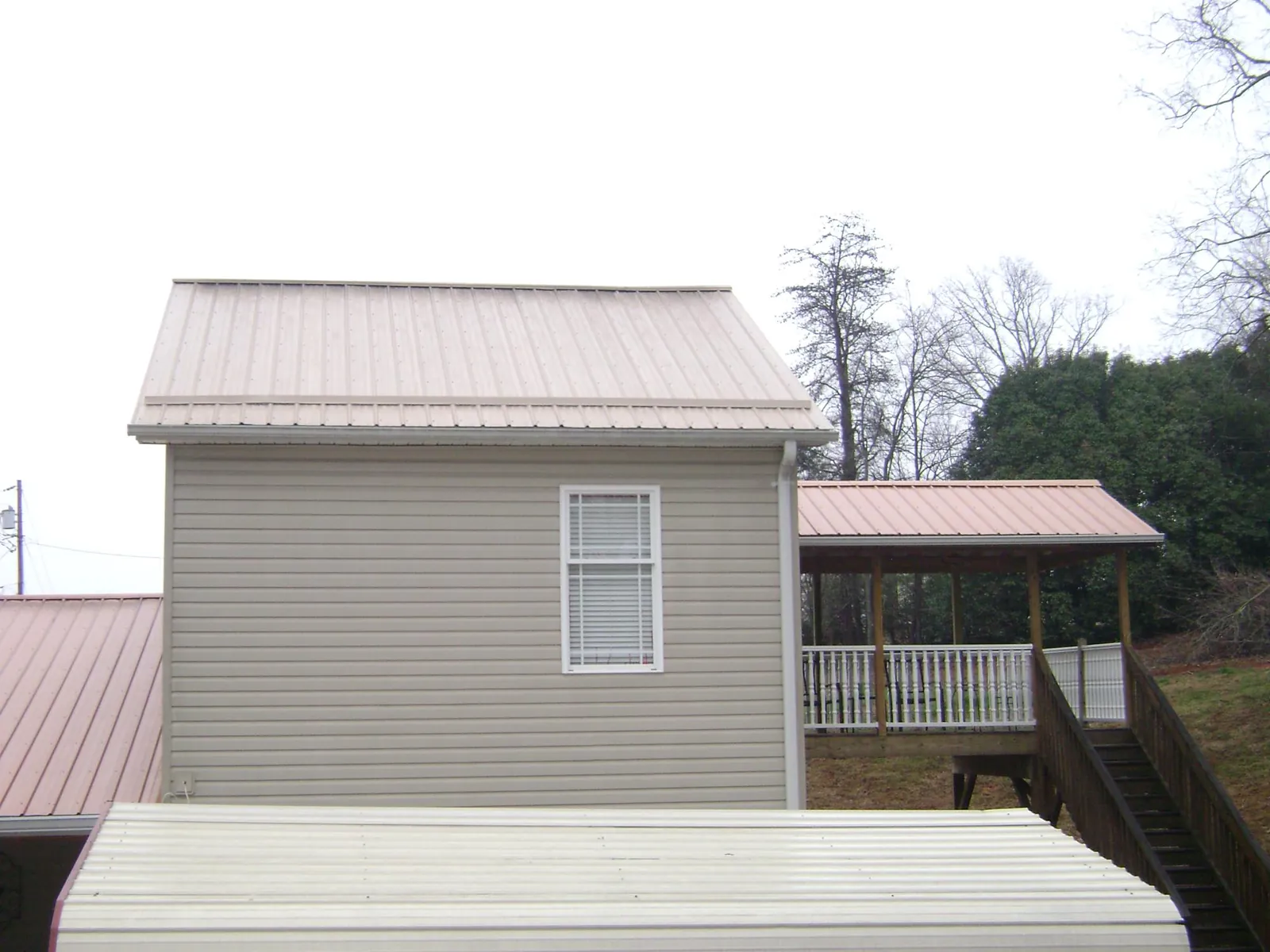Tan metal roofs on a two story addition and attached porch, from a Roof Replacement job in Woods Cross